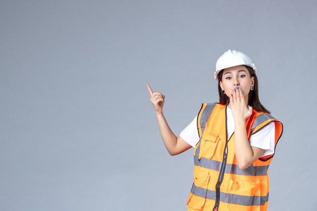 Vista frontal del constructor femenino en uniforme en la pared gris