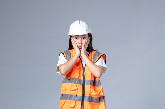 Vista frontal del constructor femenino en uniforme sorprendido en la pared blanca