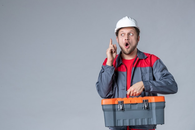 Foto gratuita vista frontal del constructor masculino en la caja de herramientas de sujeción uniforme tiene una idea sobre fondo gris