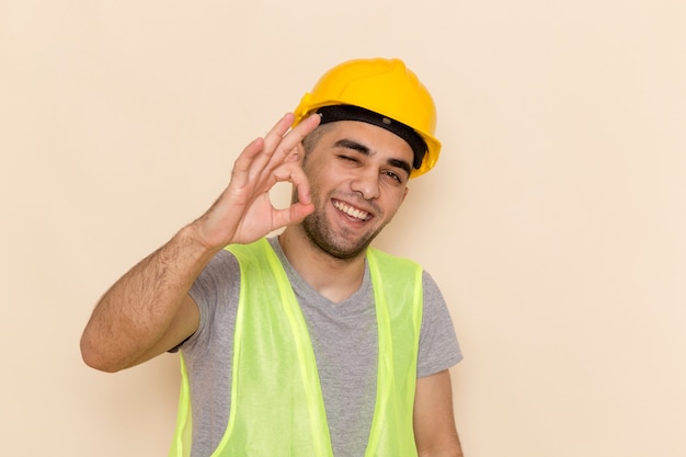 Foto gratuita vista frontal del constructor masculino en casco amarillo posando mostrando bien signo sobre fondo claro