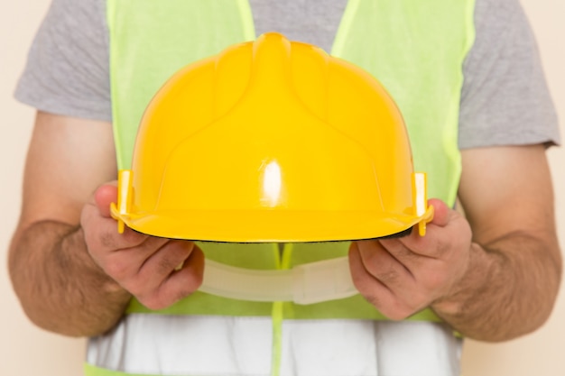 Vista frontal del constructor masculino despegando el casco amarillo sobre el fondo claro