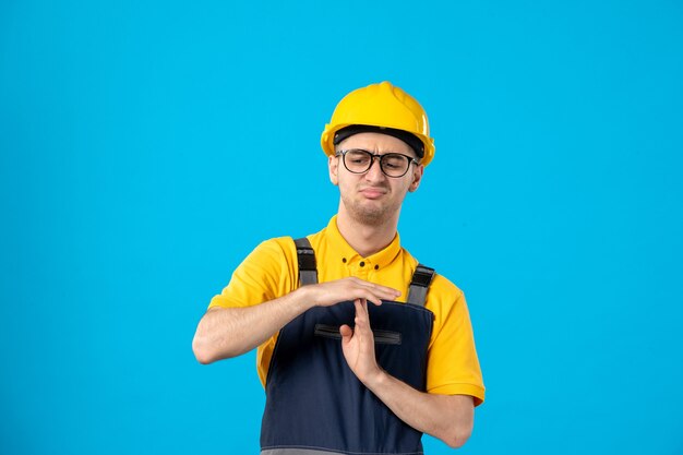 Vista frontal del constructor masculino disgustado en uniforme mostrando el signo t en una pared azul