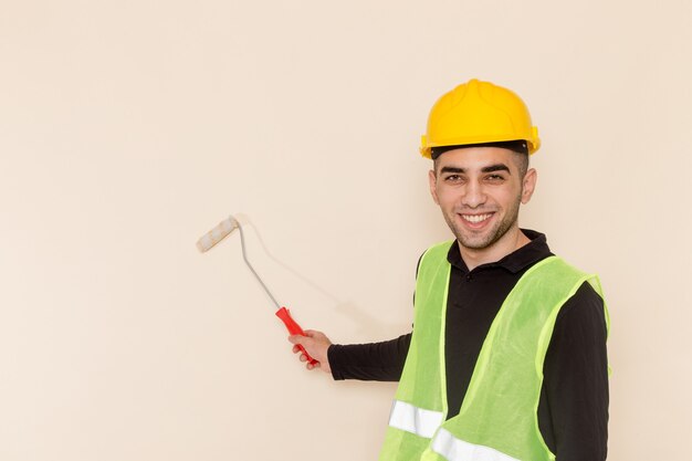 Vista frontal del constructor masculino en paredes de pintura de casco amarillo sobre el fondo claro