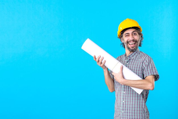 Vista frontal del constructor masculino con plan en sus manos sobre fondo azul edificio de arquitectura de ingeniero de propiedad constructor trabajador