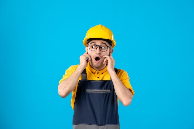 Vista frontal del constructor masculino sorprendido en uniforme sobre un azul