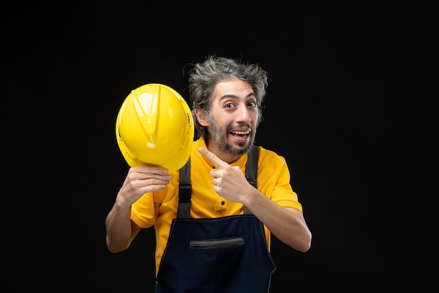 Vista frontal del constructor masculino en uniforme amarillo en la pared negra