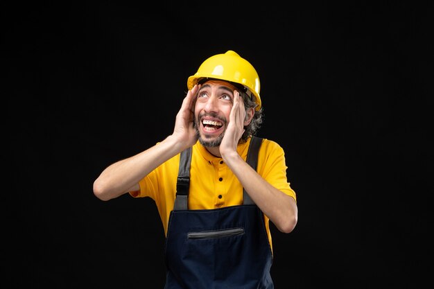 Vista frontal del constructor masculino en uniforme amarillo en la pared negra