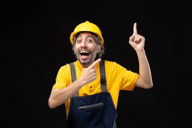 Vista frontal del constructor masculino en uniforme amarillo en la pared negra