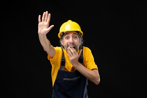 Foto gratuita vista frontal del constructor masculino en uniforme amarillo en la pared negra