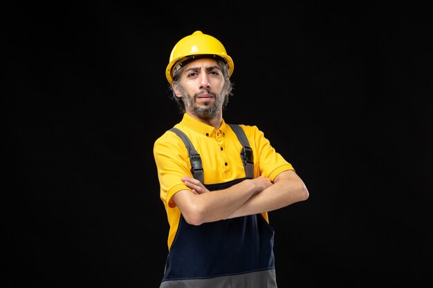 Vista frontal del constructor masculino en uniforme amarillo en la pared negra