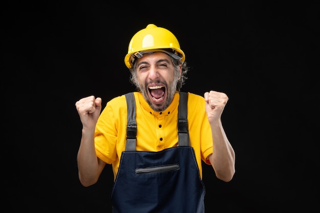 Foto gratuita vista frontal del constructor masculino en uniforme amarillo regocijándose en la pared negra