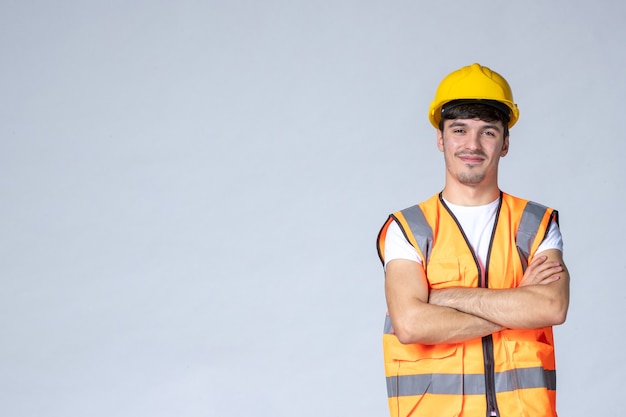 Foto gratuita vista frontal del constructor masculino en uniforme y casco amarillo en la pared blanca