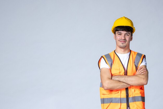 Vista frontal del constructor masculino en uniforme y casco amarillo en la pared blanca