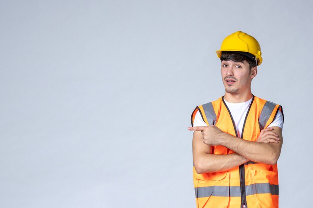 Vista frontal del constructor masculino en uniforme y casco amarillo en la pared blanca