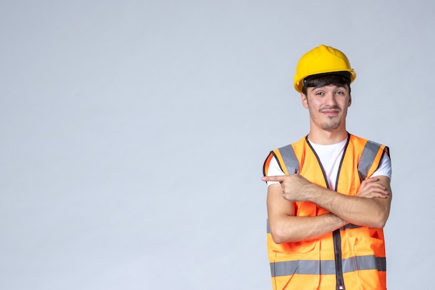 Foto gratuita vista frontal del constructor masculino en uniforme y casco amarillo sobre pared gris