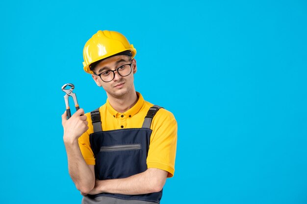 Vista frontal del constructor masculino en uniforme y casco con pinzas en la pared azul