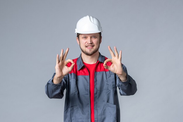 Vista frontal del constructor masculino en uniforme y casco sobre fondo gris