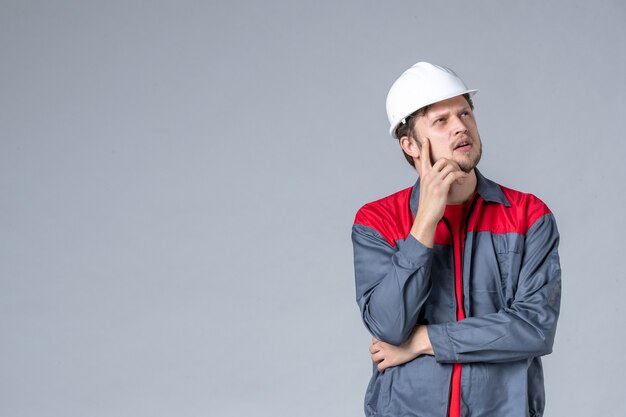 Vista frontal del constructor masculino en uniforme y casco sobre fondo gris