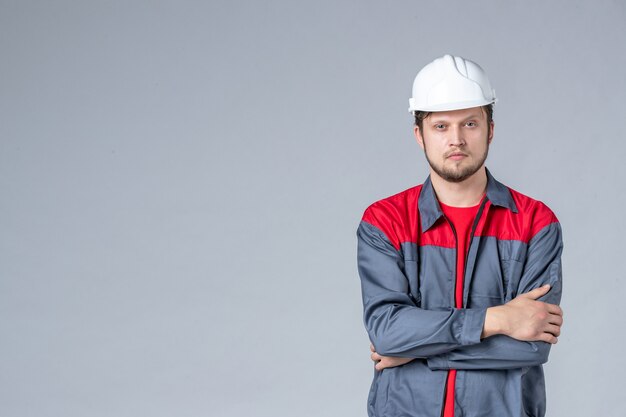 Vista frontal del constructor masculino en uniforme y casco sobre fondo gris