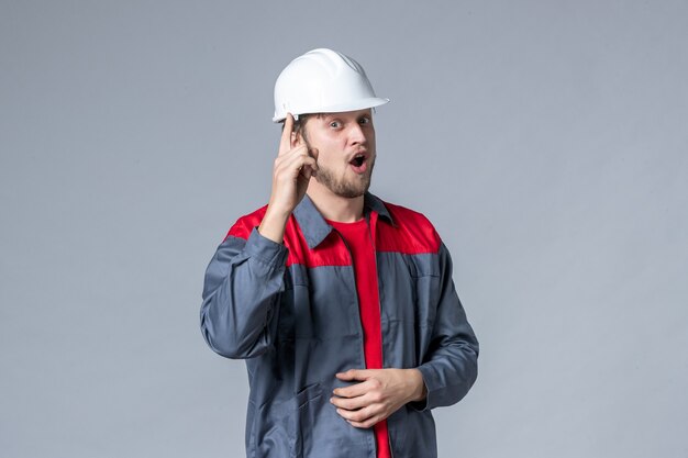 Vista frontal del constructor masculino en uniforme y casco sobre fondo gris