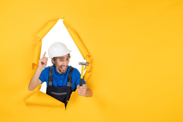 Vista frontal del constructor masculino en uniforme con un martillo en la pared amarilla color trabajador constructor de trabajo arquitectura edificio hombre
