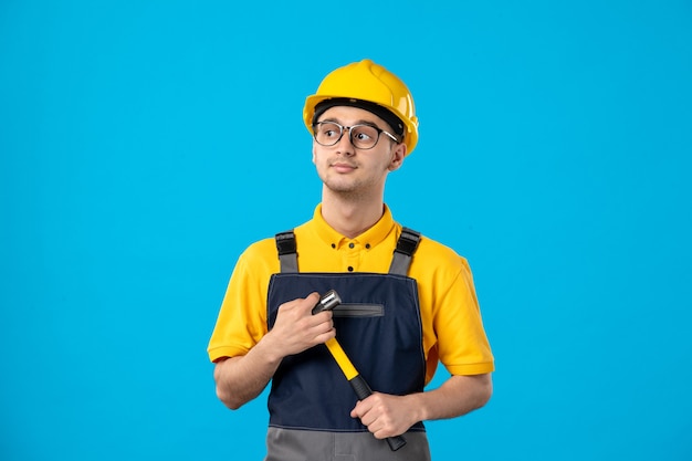 Vista frontal del constructor masculino en uniforme con un martillo en sus manos sobre la pared azul