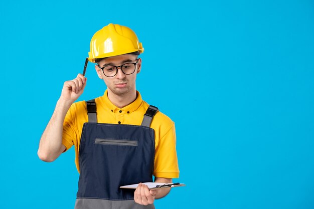 Vista frontal del constructor masculino en uniforme con nota de archivo en sus manos en la pared azul