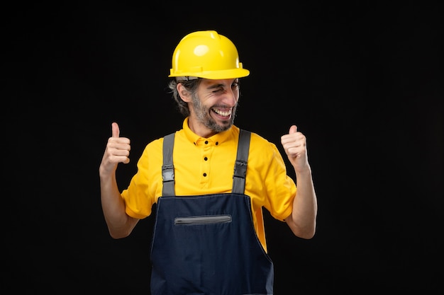 Vista frontal del constructor masculino en uniforme en la pared negra