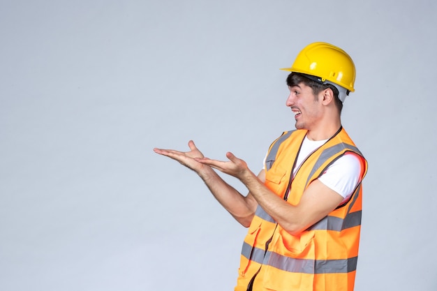 Vista frontal del constructor masculino en uniforme sonriendo a alguien en la pared blanca