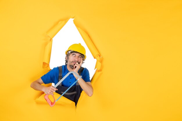 Vista frontal del constructor masculino en uniforme sosteniendo la sierra de arco sobre fondo amarillo