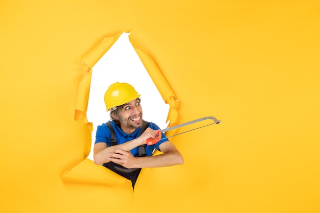 Vista frontal del constructor masculino en uniforme sosteniendo la sierra de arco sobre fondo amarillo
