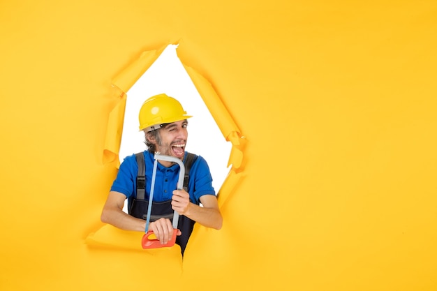 Vista frontal del constructor masculino en uniforme sosteniendo la sierra de arco sobre fondo amarillo