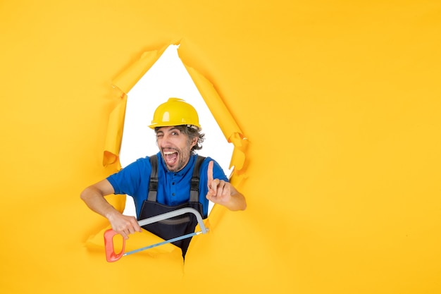 Vista frontal del constructor masculino en uniforme sosteniendo la sierra de arco sobre fondo amarillo