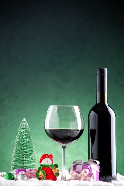 Vista frontal copa de vino y una botella de adornos navideños sobre fondo verde
