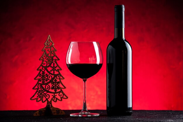 Vista frontal de la copa de vino y una botella sobre fondo rojo claro