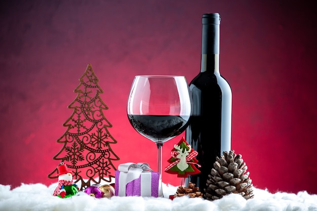 Vista frontal de una copa de vino botella de vino decoraciones navideñas piña sobre fondo rojo oscuro