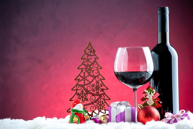 Vista frontal de la copa de vino y detalles de Navidad de botella sobre fondo rojo oscuro