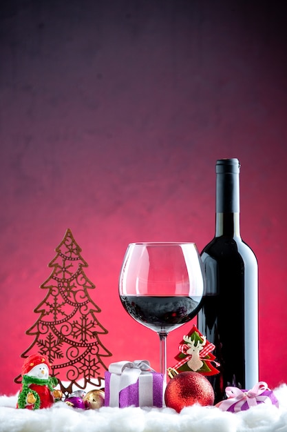 Vista frontal de la copa de vino y detalles de Navidad de botella sobre fondo rojo oscuro
