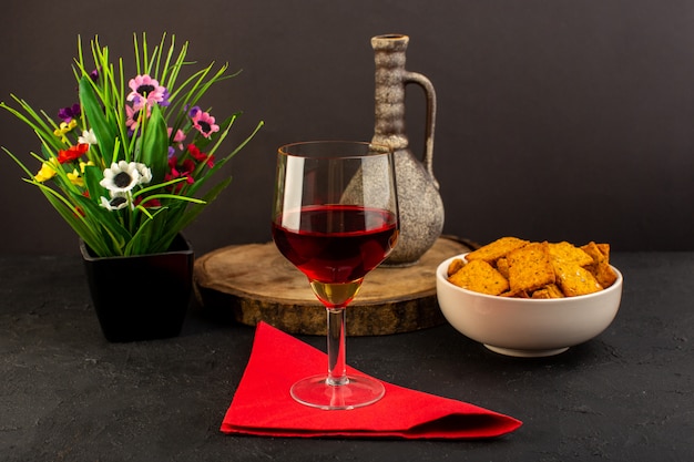 Vista frontal de una copa de vino junto con flores y patatas fritas dentro de la placa en el escritorio oscuro