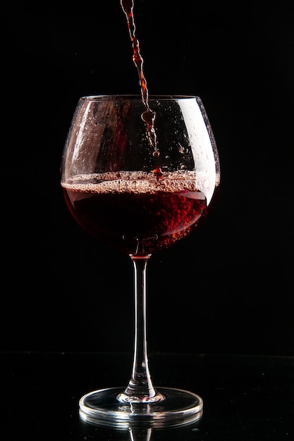 Foto gratuita vista frontal de la copa de vino que se vierte con vino tinto en bebida de color negro, champán, alcohol de navidad