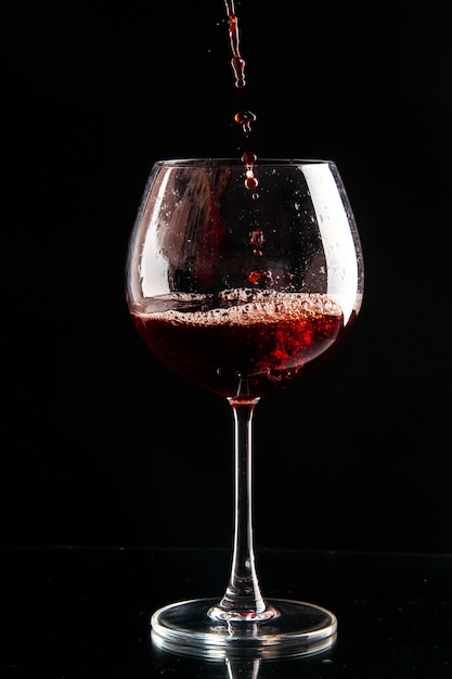 Vista frontal de la copa de vino que se vierte con vino tinto en bebida de color negro, champán, alcohol de Navidad