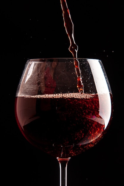 Vista frontal de la copa de vino que se vierte con vino tinto en color negro champagne bebida alcohólica de navidad