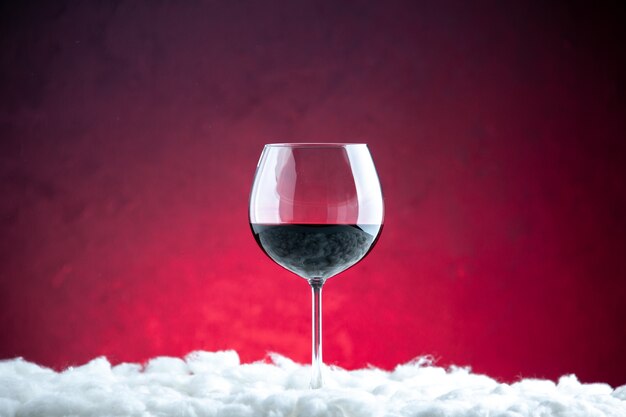 Vista frontal de una copa de vino sobre fondo rojo oscuro