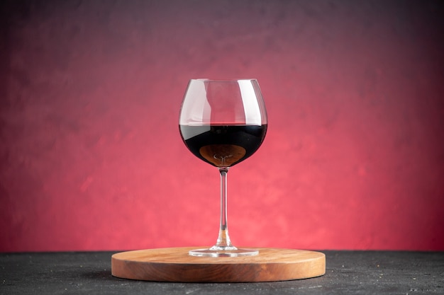 Vista frontal de la copa de vino tinto sobre tablero de madera sobre fondo rojo.