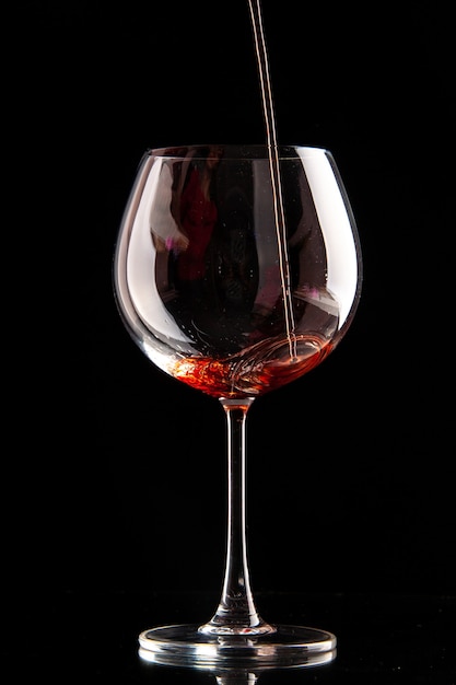 Vista frontal de la copa de vino se vierte con vino tinto sobre alcohol de Navidad de champán de color negro