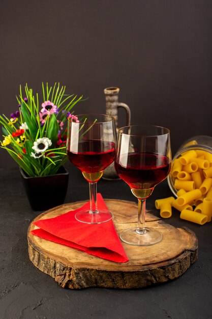 Una vista frontal copas de vino en un escritorio de madera marrón junto con flores y pasta italiana cruda en un escritorio oscuro