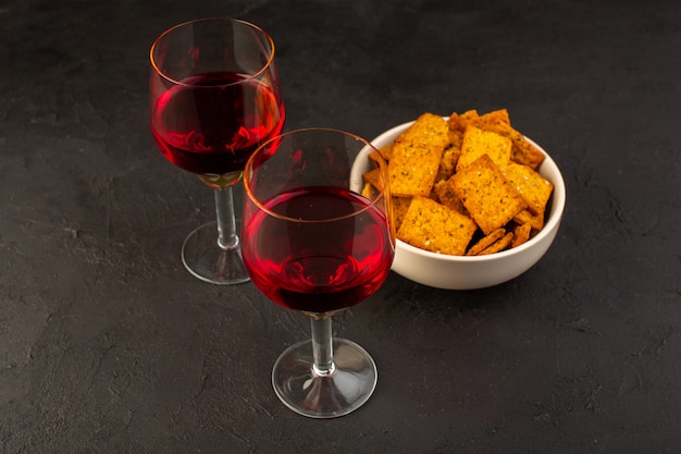 Una vista frontal de copas de vino junto con patatas fritas dentro de la placa en la oscuridad