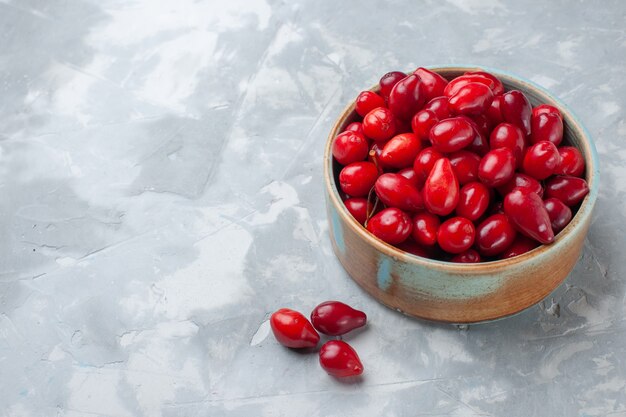 Vista frontal de cornejos frescos rojos frutas agrias y deliciosas dentro de la olla en la mesa de luz fruta fresca agria suave