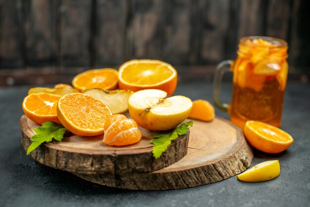 Vista frontal cortar manzanas y naranjas en cóctel de tablero de madera sobre fondo oscuro