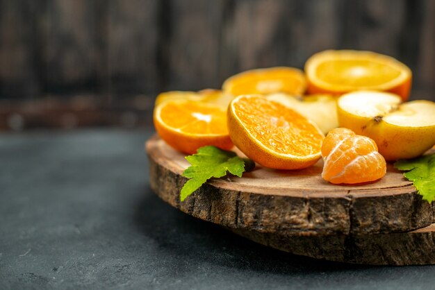 Vista frontal cortar manzanas y naranjas sobre tablero de madera en la oscuridad